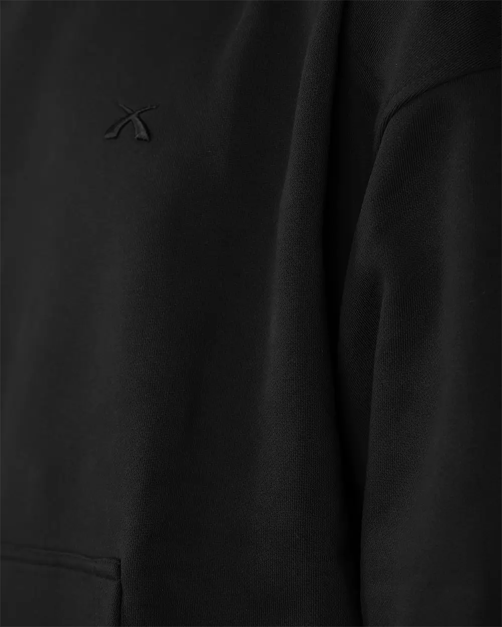Makro-Detailaufnahme des hochwertigen, Ton-in-Ton gehaltenen 3D-Logo-Sticks auf der Brust des schwarzen SQUEQO Oversized Hoodies.