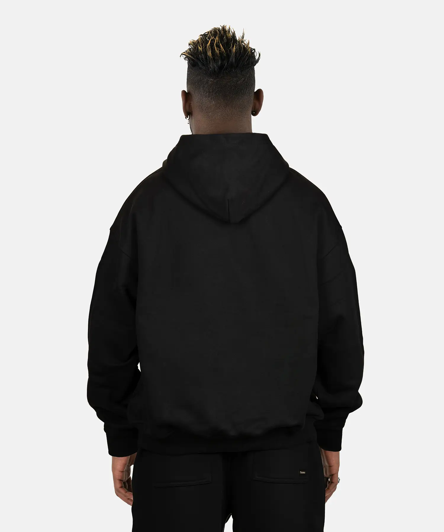 Rückansicht des schwarzen SQUEQO Oversized Hoodies, getragen von einem Model. Die cleane Rückenpartie und die Crossover-Kapuze werden gezeigt.