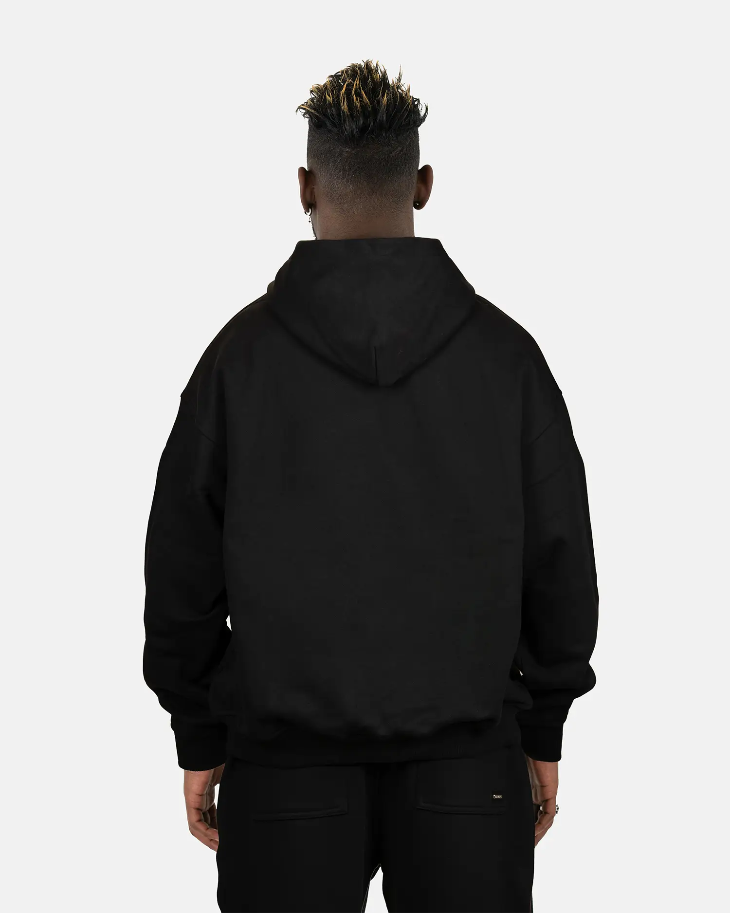 Rückansicht des schwarzen SQUEQO Oversized Hoodies, getragen von einem Model. Die cleane Rückenpartie und die Crossover-Kapuze werden gezeigt.
