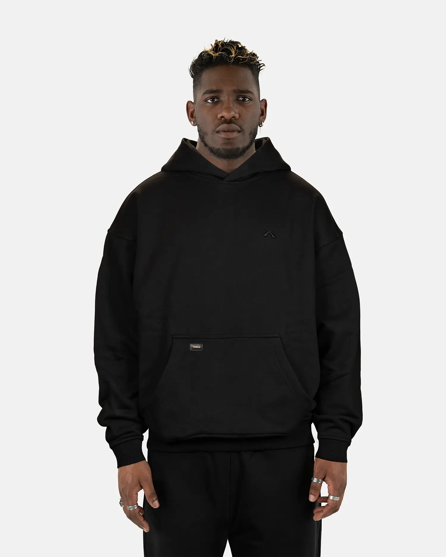 Model präsentiert den schwarzen SQUEQO Oversized Hoodie in der Unisex-Passform von vorne. Die Drop-Shoulder-Silhouette und der dezente 3D-Logo-Stick sind deutlich zu sehen.