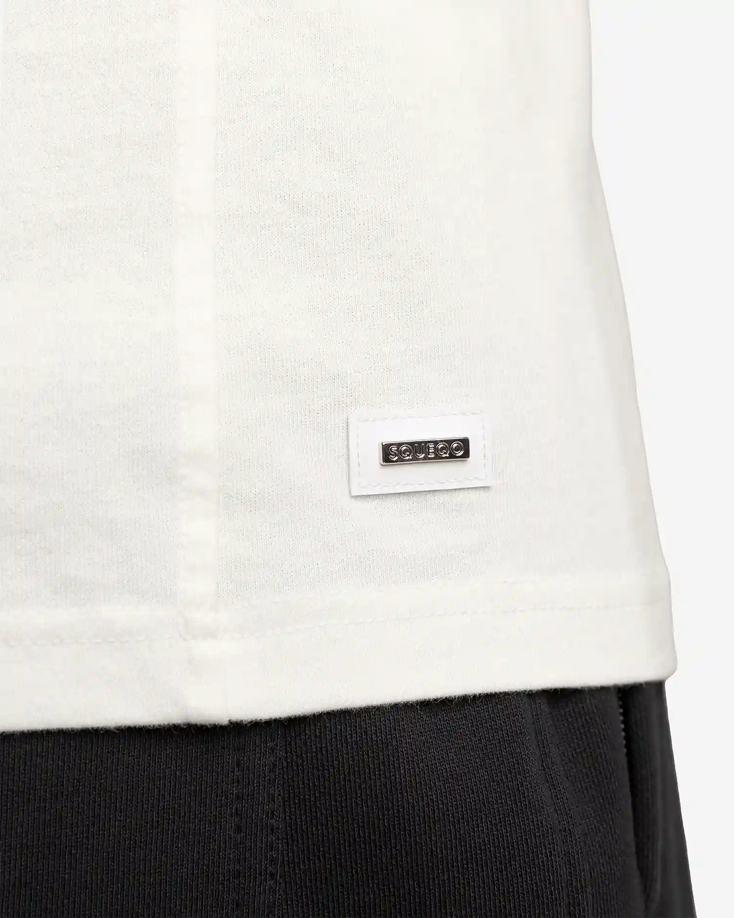 Nahaufnahme des gewebten Squeqo Logo-Labels am Saum des Off-White Basic T-Shirts.