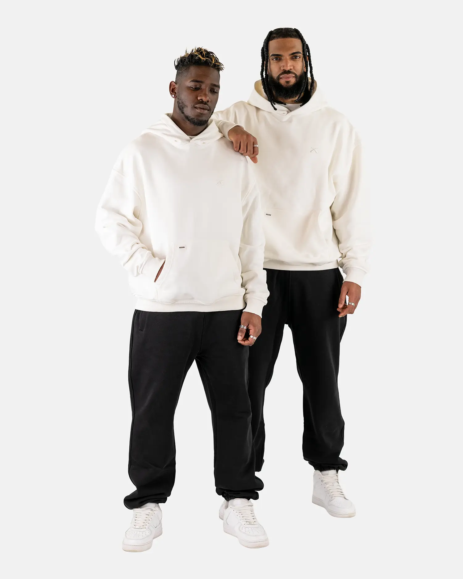 Zwei männliche Models tragen den Squeqo Essential Oversized Hoodie in Off-White zu schwarzen Hosen.