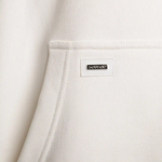 Detailaufnahme des Squeqo Metall-Patches an der Kängurutasche des Hoodies.