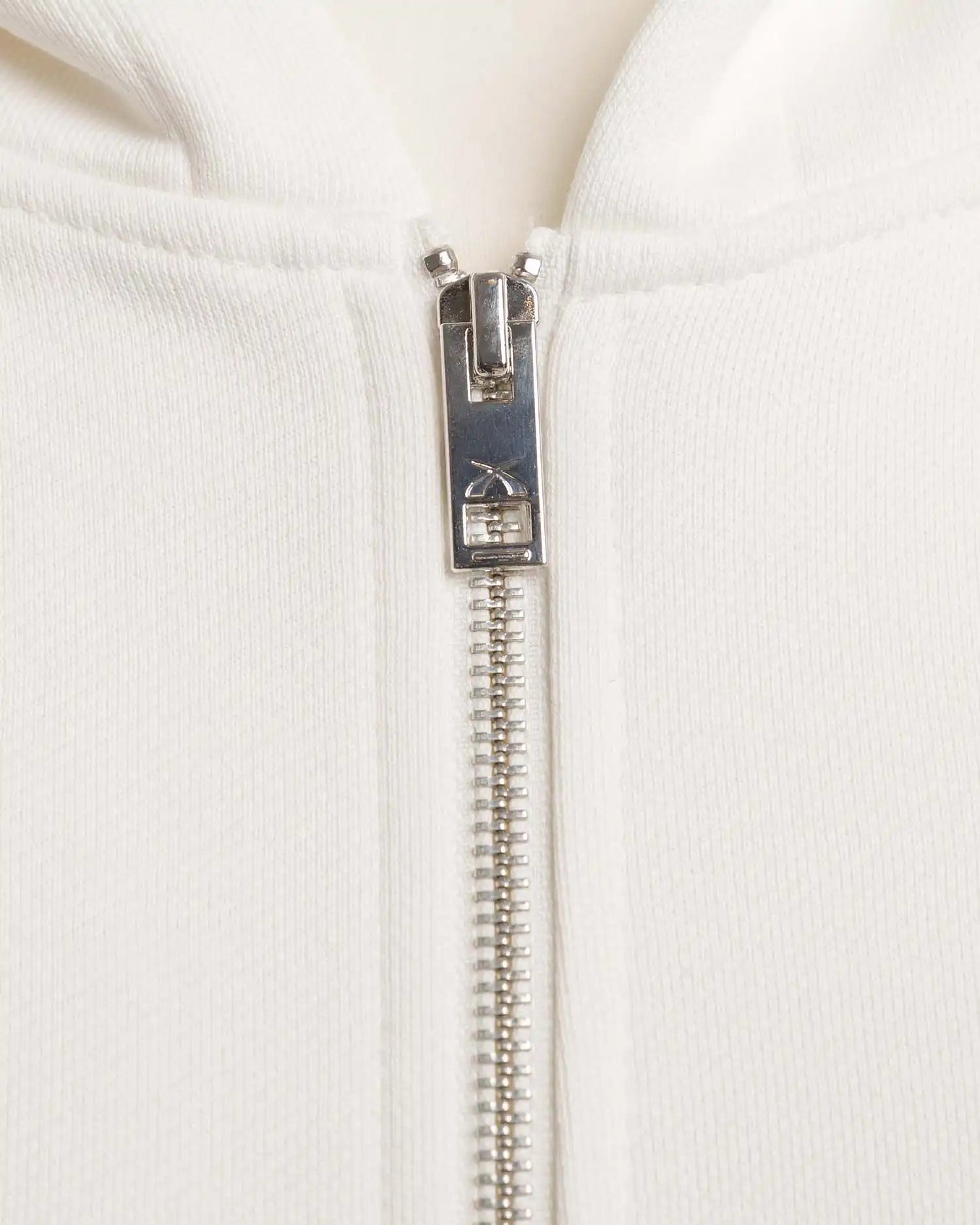 Nahaufnahme des YKK Zwei-Wege-Reißverschlusses mit Squeqo-Logo am Essential Zip Hoodie.