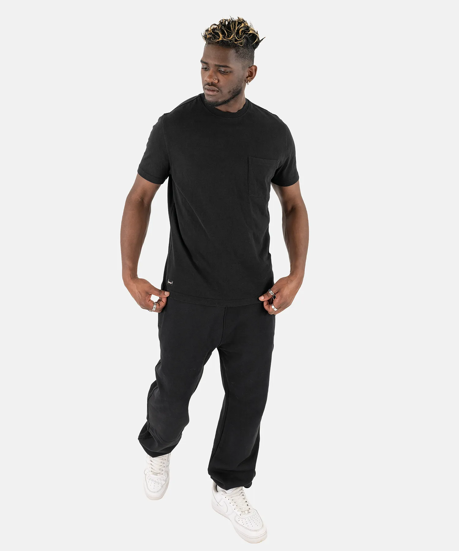 Ein männliches Model in einem kompletten schwarzen Outfit mit dem Squeqo Essential Pocket T-Shirt.