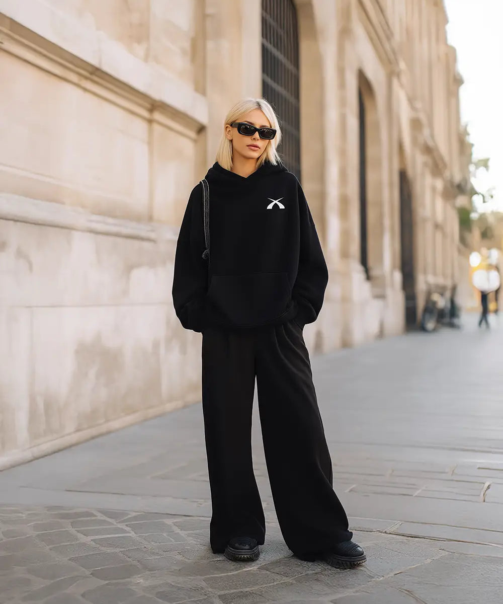 Model trägt den schwarzen SQUEQO Oversized Icon Hoodie (Fit 02) in einem urbanen Street-Style-Look.