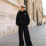 Model trägt den schwarzen SQUEQO Oversized Icon Hoodie (Fit 02) in einem urbanen Street-Style-Look.