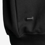 Detailansicht: SQUEQO Metall-Logo-Patch am Saum des Sweatshirts