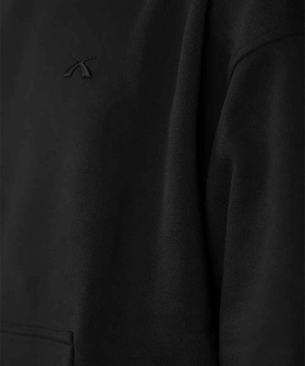 Makro-Detailaufnahme des hochwertigen, Ton-in-Ton gehaltenen 3D-Logo-Sticks auf der Brust des schwarzen SQUEQO Oversized Hoodies.