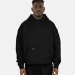 Model präsentiert den schwarzen SQUEQO Oversized Hoodie in der Unisex-Passform von vorne. Die Drop-Shoulder-Silhouette und der dezente 3D-Logo-Stick sind deutlich zu sehen.