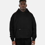 Model präsentiert den schwarzen SQUEQO Oversized Hoodie in der Unisex-Passform von vorne. Die Drop-Shoulder-Silhouette und der dezente 3D-Logo-Stick sind deutlich zu sehen.