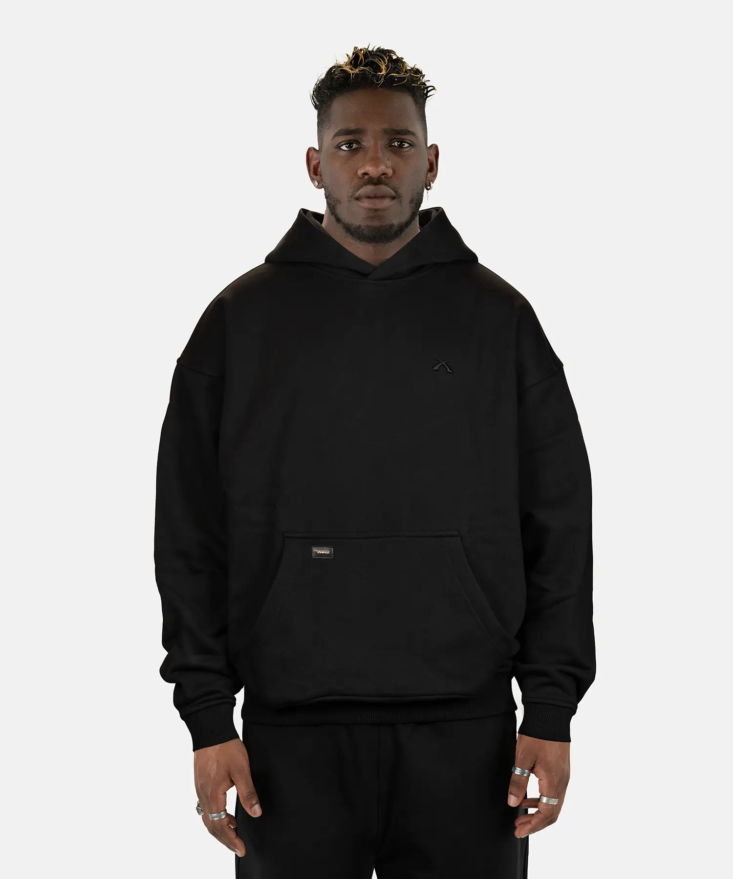 Model präsentiert den schwarzen SQUEQO Oversized Hoodie in der Unisex-Passform von vorne. Die Drop-Shoulder-Silhouette und der dezente 3D-Logo-Stick sind deutlich zu sehen.