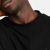 Detailaufnahme des SQUEQO T-Shirts in Schwarz, die das hochwertige, Ton-in-Ton gestickte Logo auf der Brust und den robusten Kragen hervorhebt.
