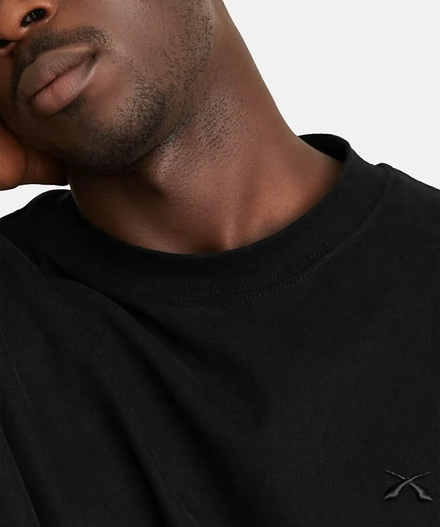 Detailaufnahme des SQUEQO T-Shirts in Schwarz, die das hochwertige, Ton-in-Ton gestickte Logo auf der Brust und den robusten Kragen hervorhebt.