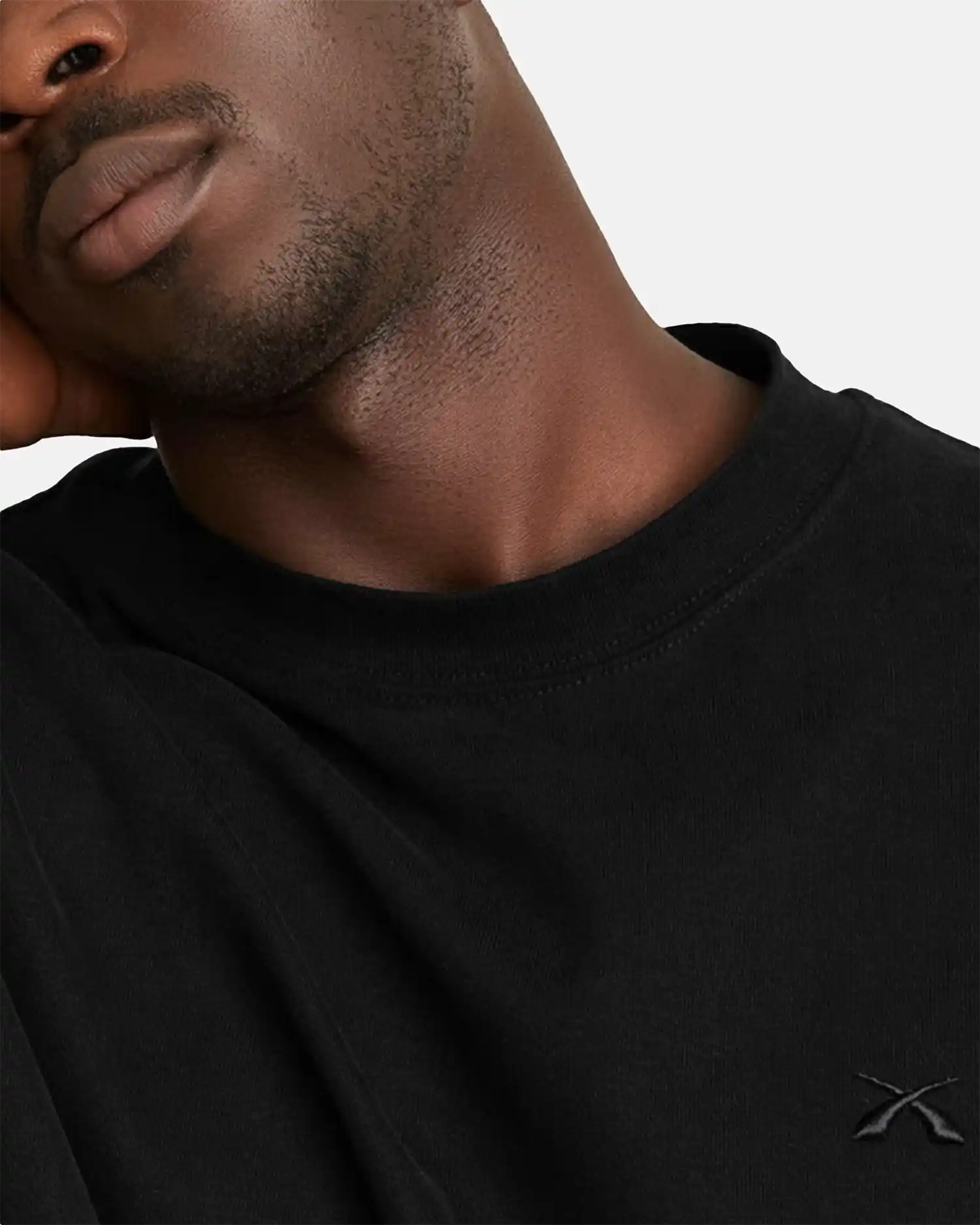 Detailaufnahme des SQUEQO T-Shirts in Schwarz, die das hochwertige, Ton-in-Ton gestickte Logo auf der Brust und den robusten Kragen hervorhebt.