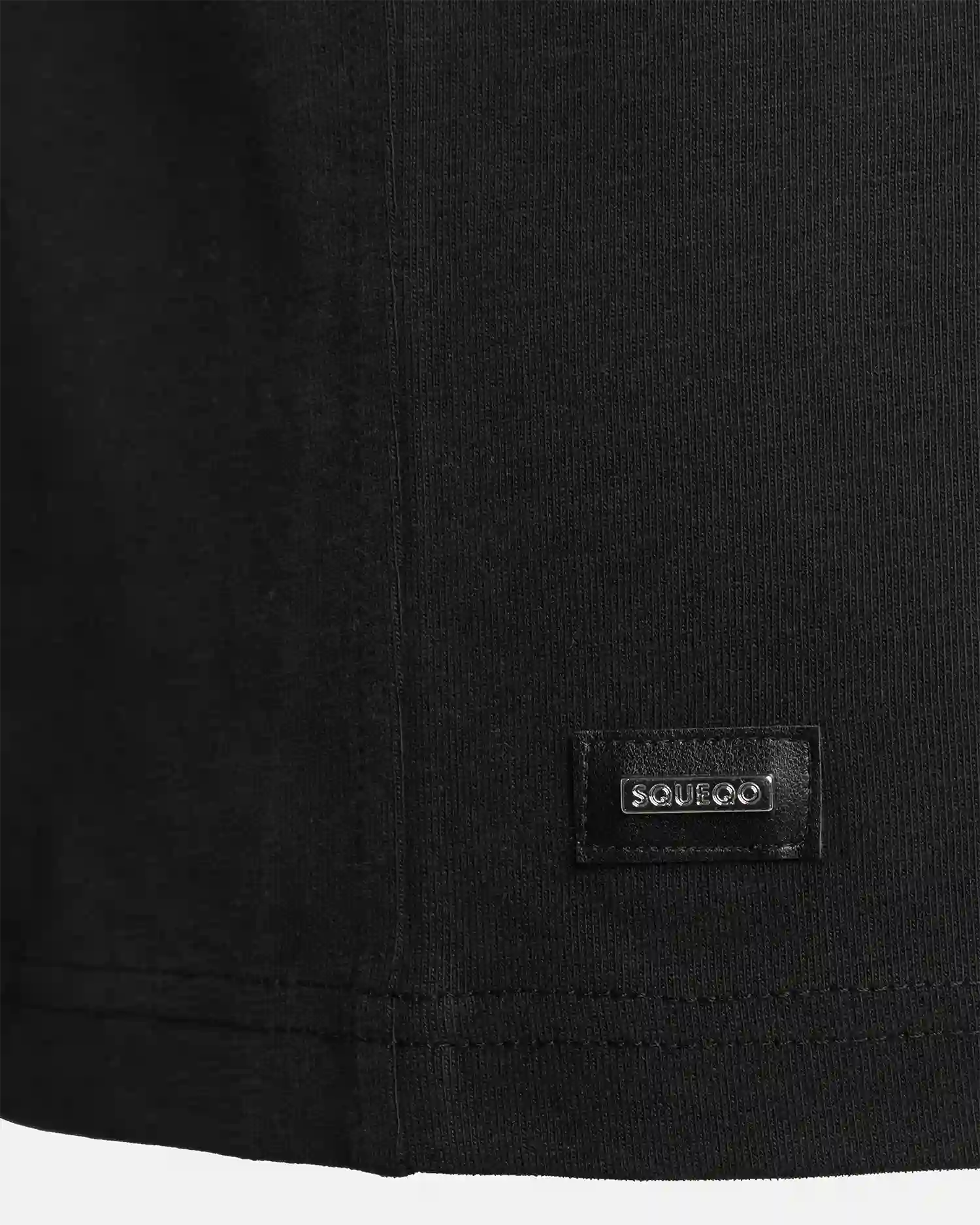 Detailaufnahme des SQUEQO T-Shirts in Schwarz, die das hochwertige, Ton-in-Ton gestickte Logo auf der Brust und den robusten Kragen hervorhebt.