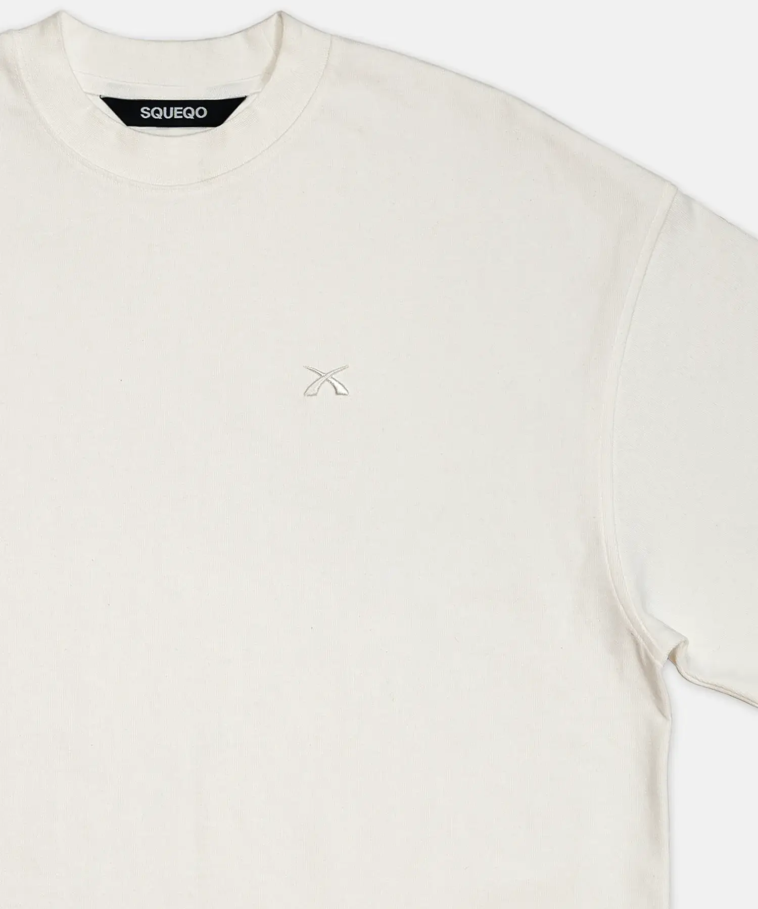 Detailaufnahme des SQUEQO T-Shirts in Off-White, die die doppelt verstärkten Nähte am Ärmel und die hochwertige Logo-Stickerei auf der Brust zeigt.